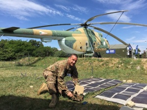 soldier in front of a helicopter with a foldable solar panel connected to a battery